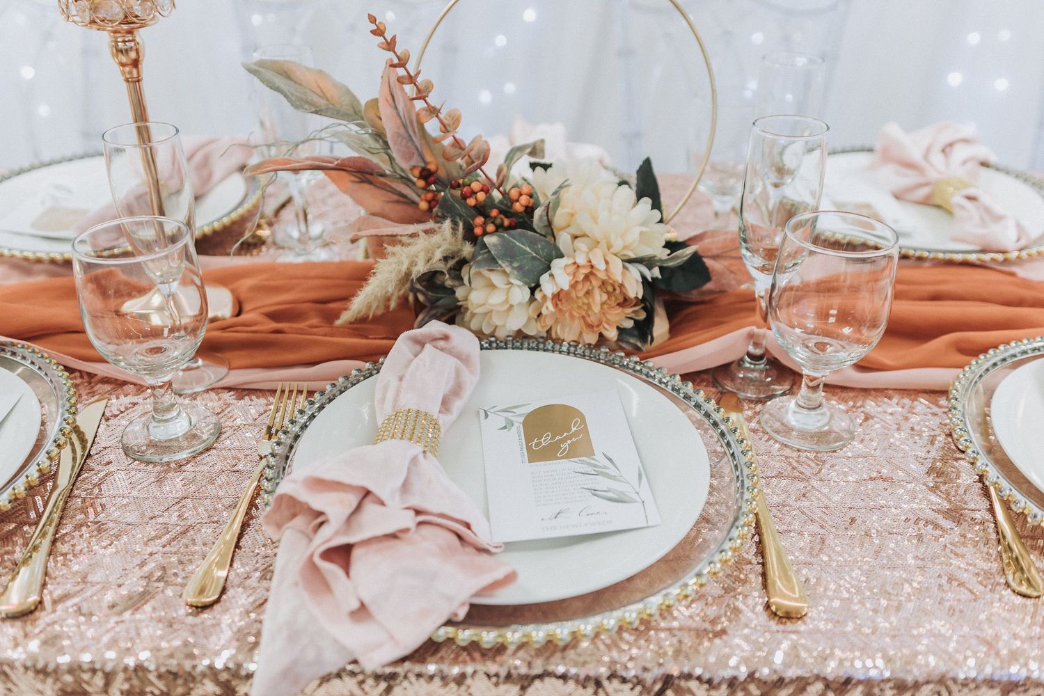 Romantic table setting with rose gold linens, gold flatware, and delicate floral centerpiece.