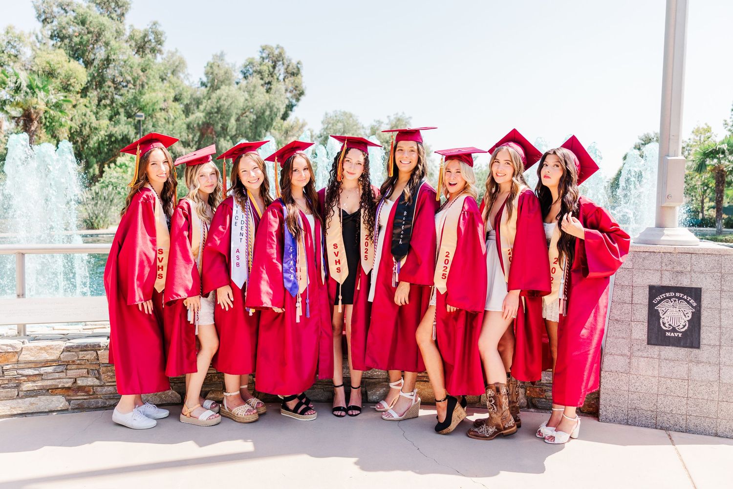 Group in vibrant red graduation gowns poses together outdoors on stone steps for celebratory photo shoot.