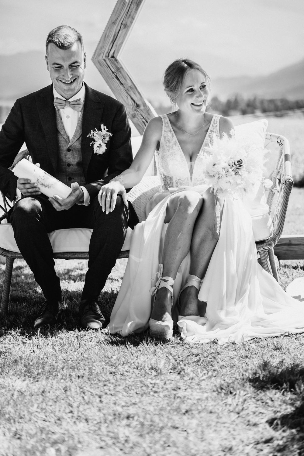 Black and white panorama of wedding couple sitting on grassy hill showing four sequential poses from left to right.