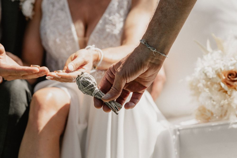 A close-up shot of hands opening a wine bottle next to a white wedding dress and floral bouquet.