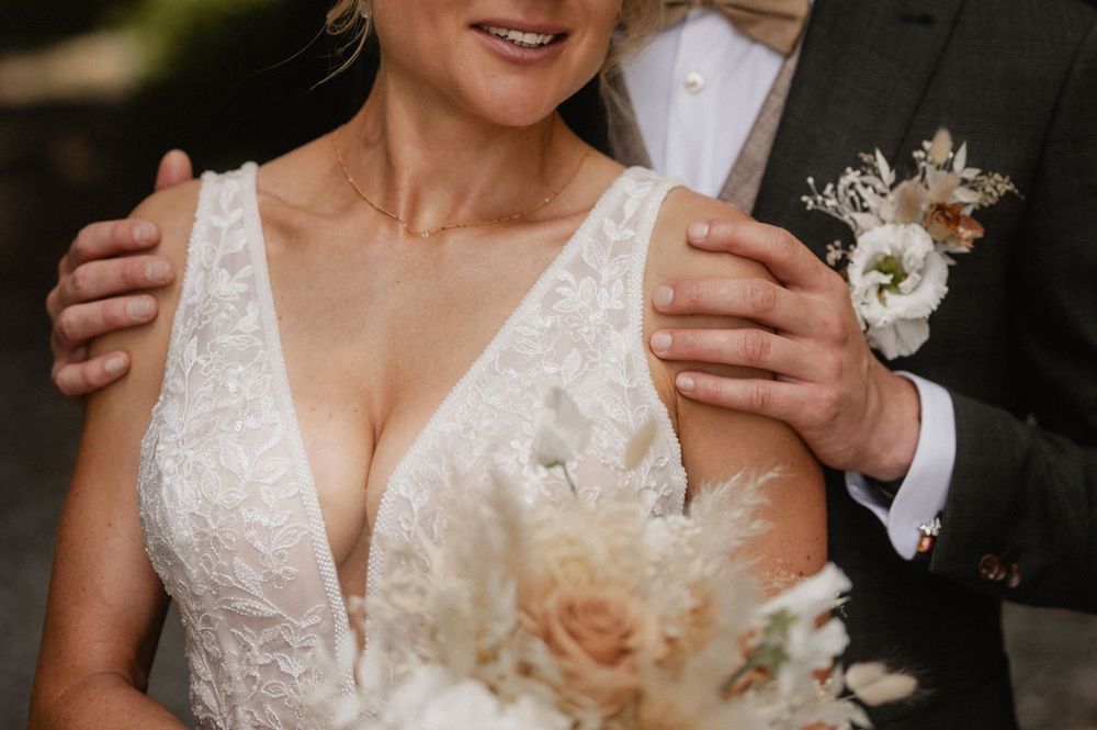 Bride and groom pose together during their celebration while showcasing elegant lace wedding dress details.