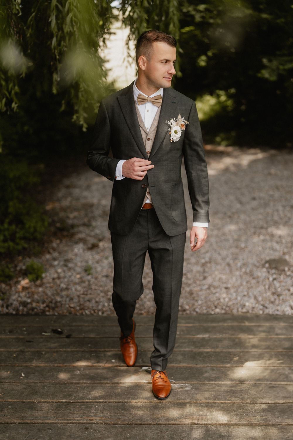 Close-up shots of groom's brown leather dress shoes and suit pants while walking on wooden deck.