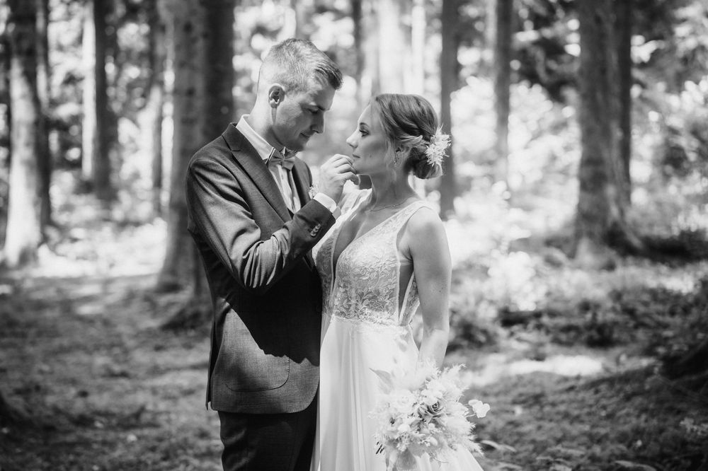 A couple shares an intimate moment while dancing together in a wooded forest setting.