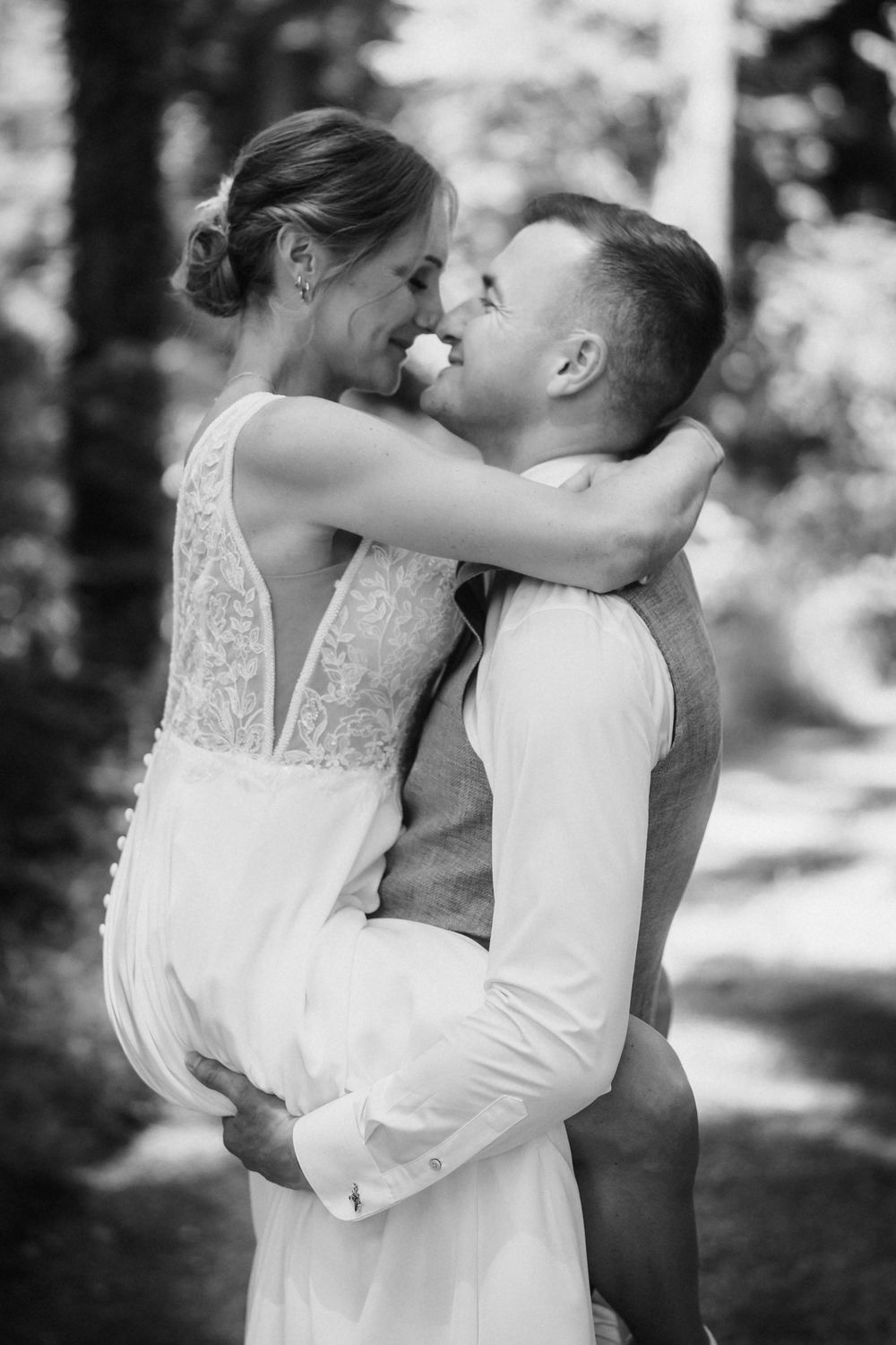 A tender black and white wedding photo of the newlyweds sharing an intimate embrace in a forest setting.