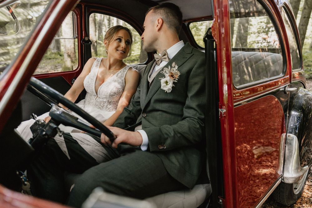 A couple in wedding attire share an intimate moment inside a vintage red car.