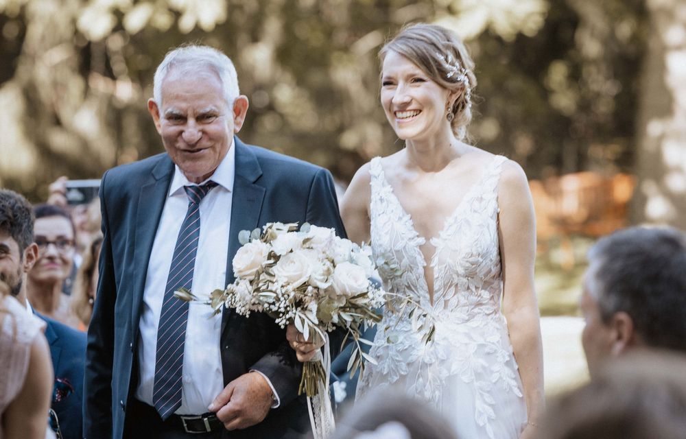 A bride in a plunging neckline lace dress walks down the aisle carrying a neutral-toned bouquet.