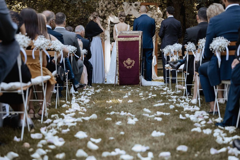 White rose petals line a rustic outdoor wedding ceremony aisle with chairs and guests in attendance.