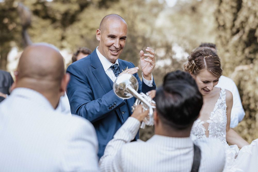 A cheerful celebration moment at an outdoor wedding ceremony with guests gathered together in sunlit natural surroundings.