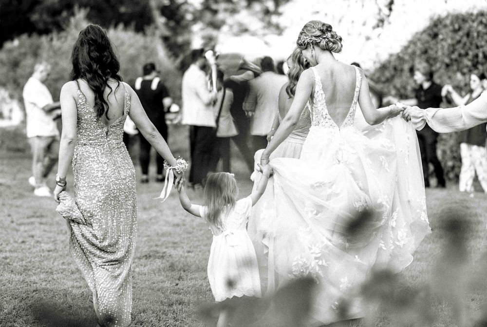 Black and white photo of wedding guests dancing outdoors on a grassy field.