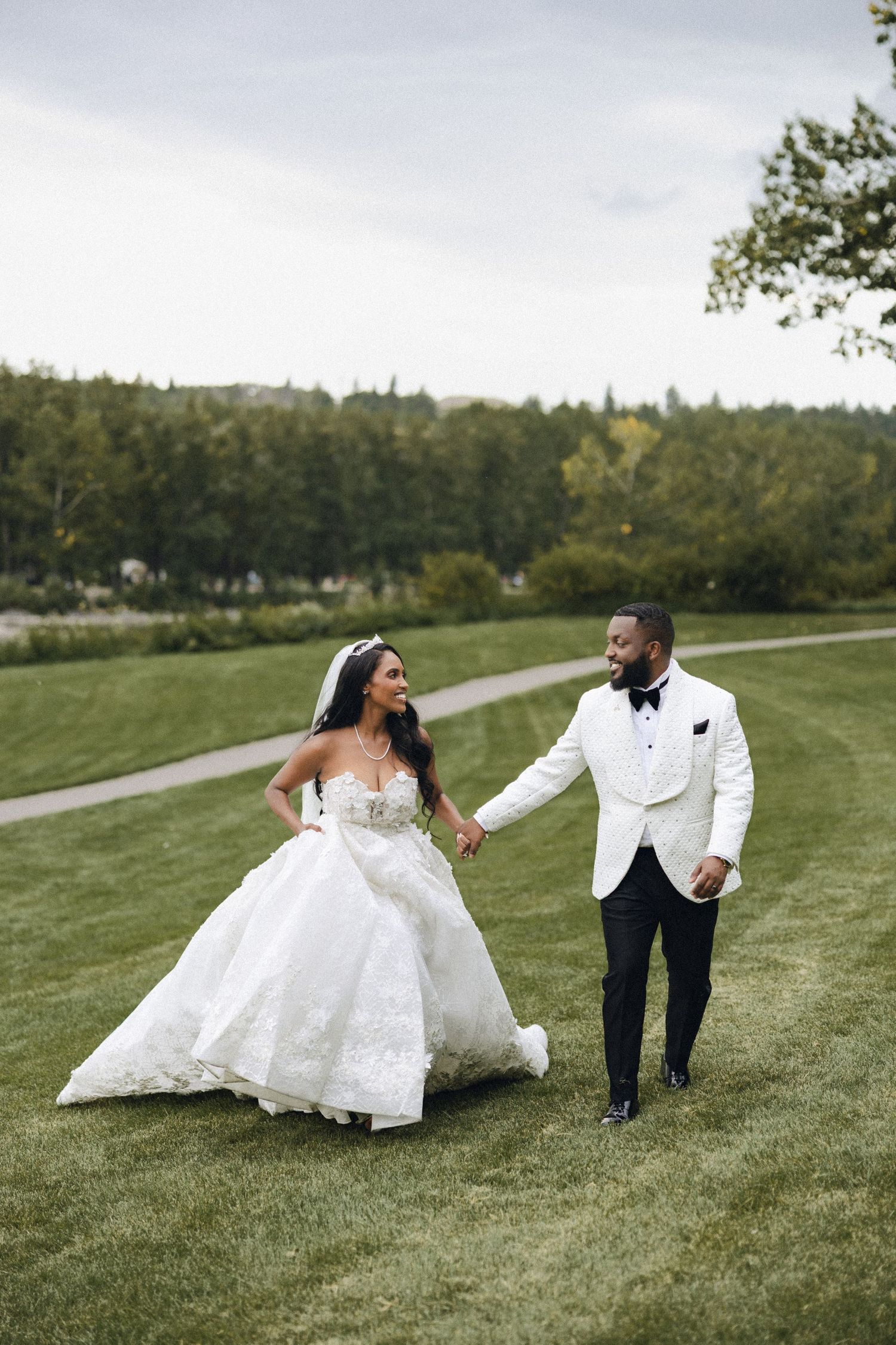 A couple shares an embrace on a lush green hillside overlooking a scenic waterfront view on their wedding day.