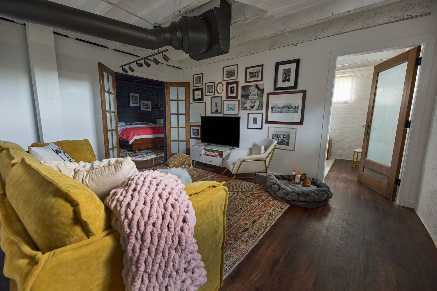 Modern living space with yellow sofa, pink throw blanket, and gallery wall of framed photos.