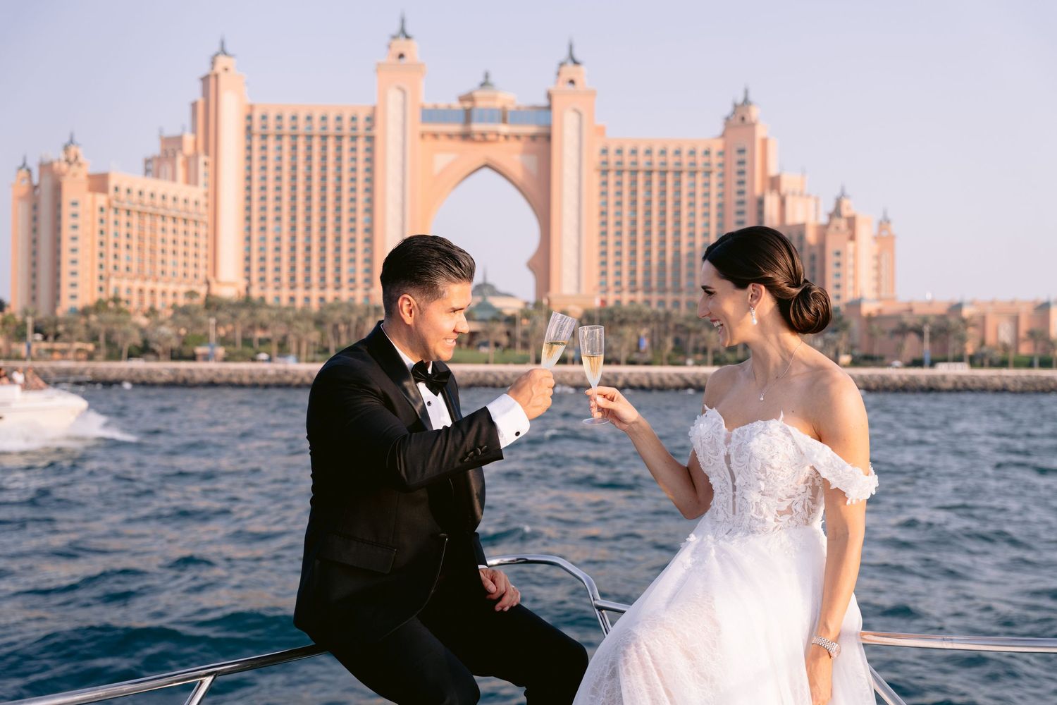Romantic wedding moment under a floral arch with pink and white blooms as newlyweds embrace in elegant attire.