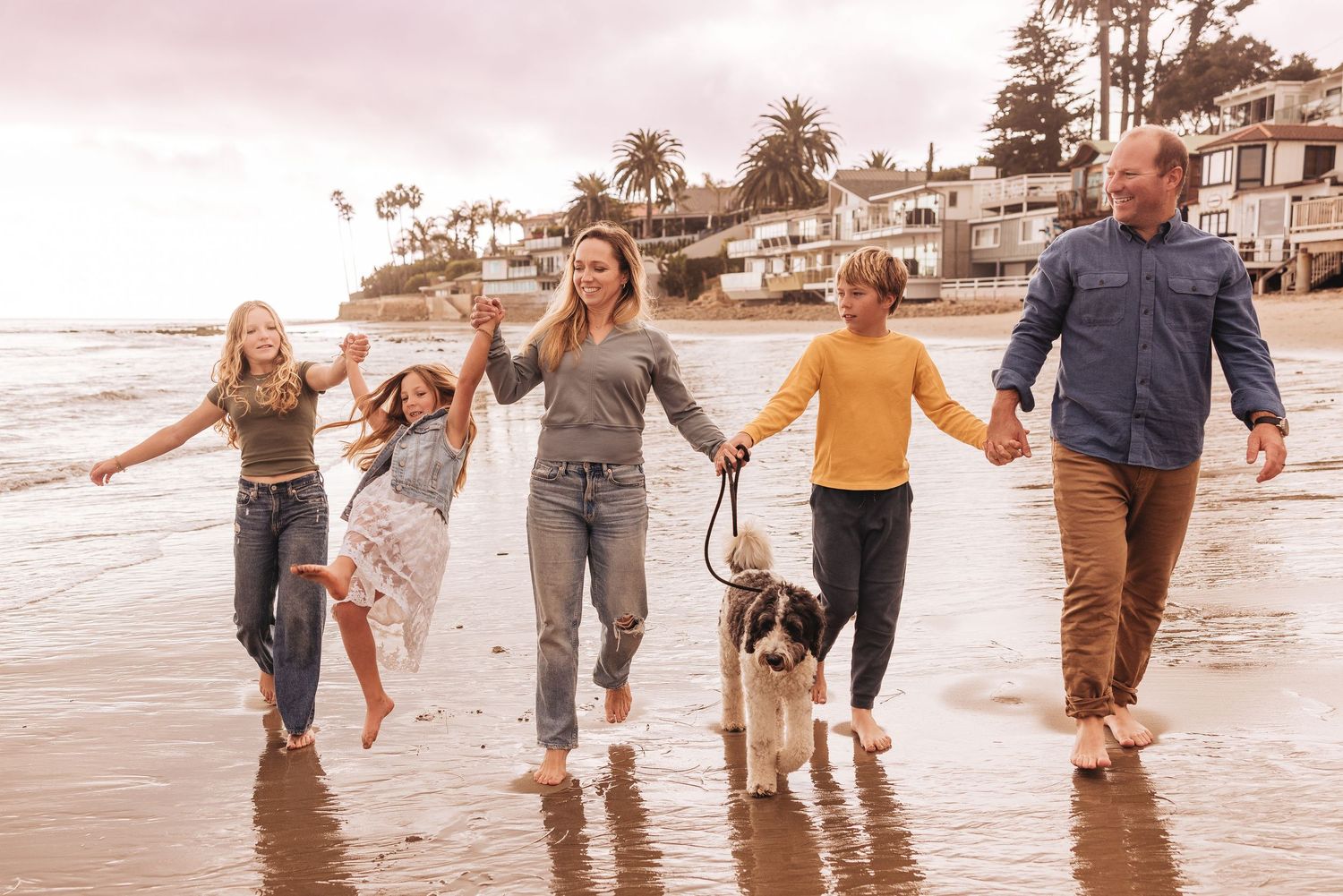 Group walking joyfully through ocean waves at sunset along sandy beach holding hands together.