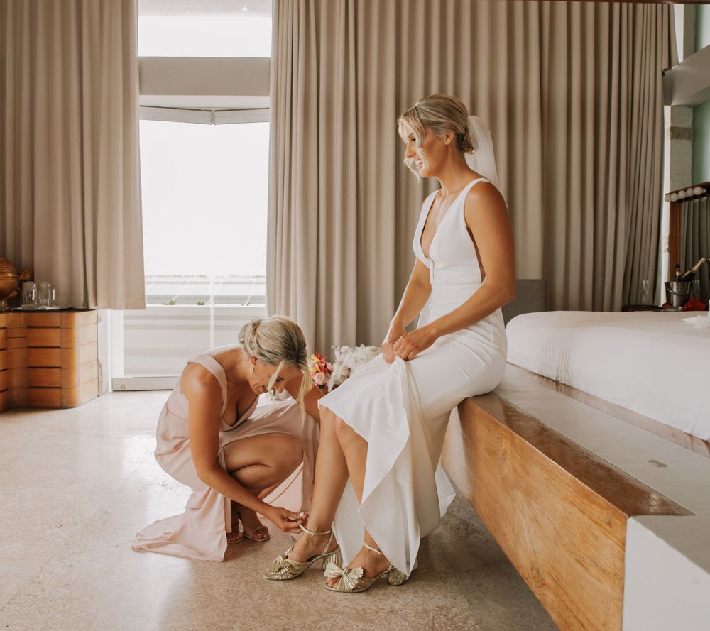 A serene moment captured in a sunlit room with flowing white dresses and delicate pre-wedding preparations.