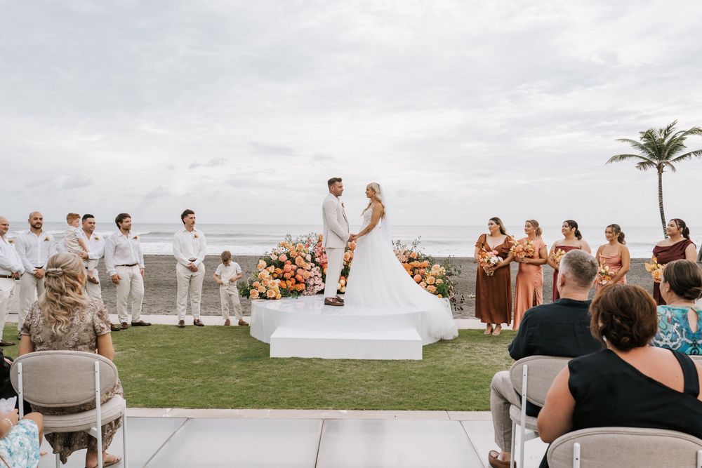 Wedding reception showing decorated outdoor tables, palm trees, and guests celebrating near the ocean.