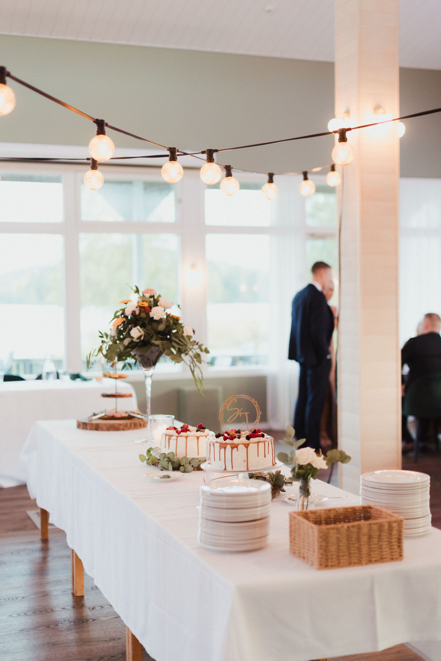 Wedding reception buffet table with white linens and floral centerpieces under string lights.