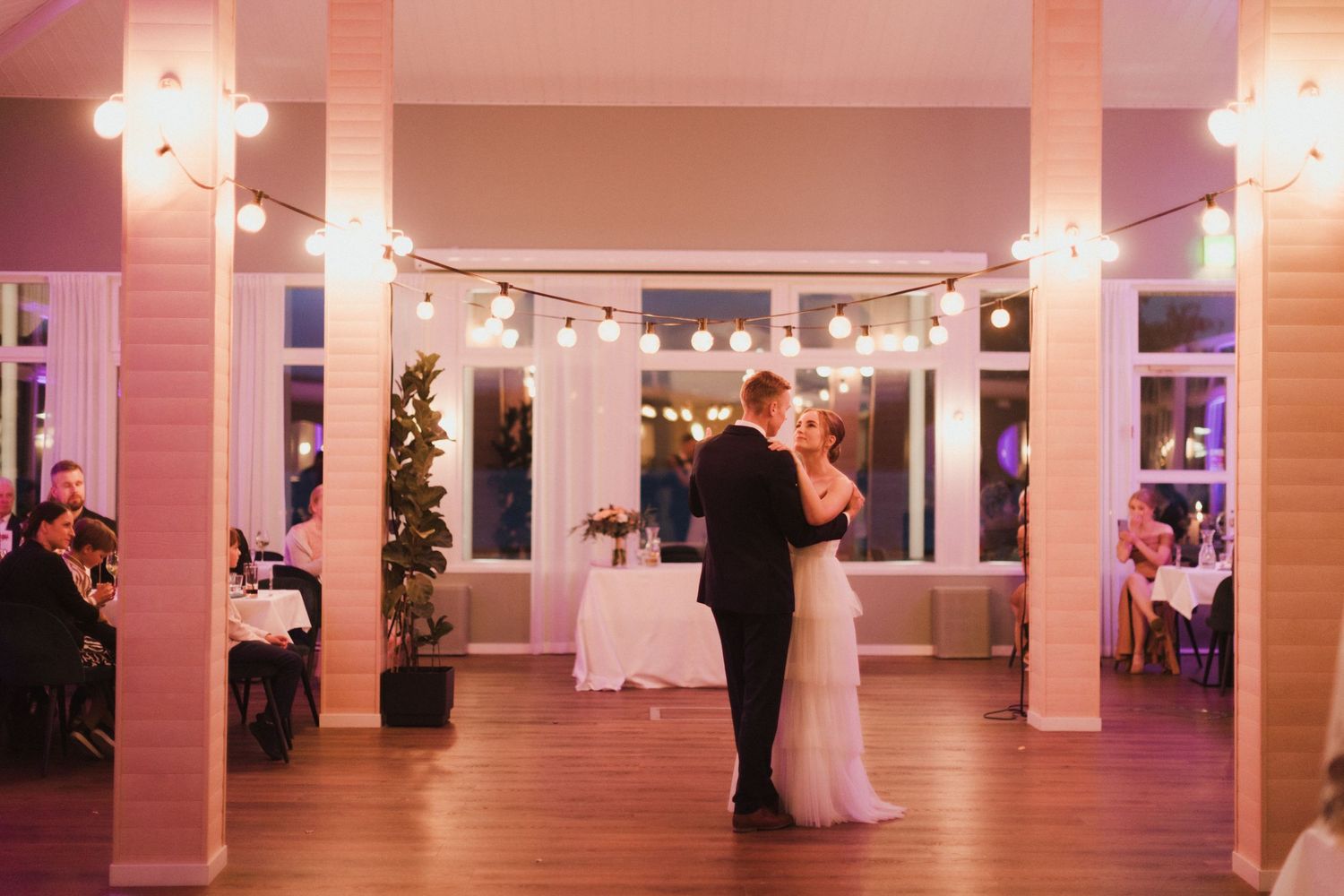 Spacious wedding reception hall with string lights and couples dancing in the distance.