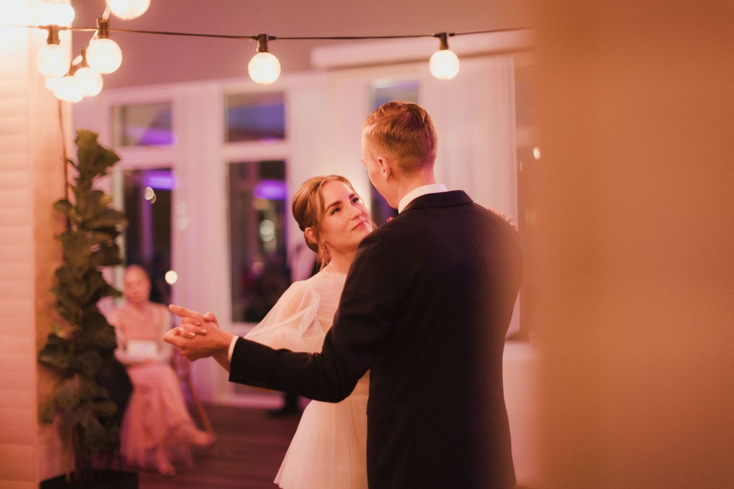 Wedding reception dance floor with string lights and couples dancing in warm lighting.