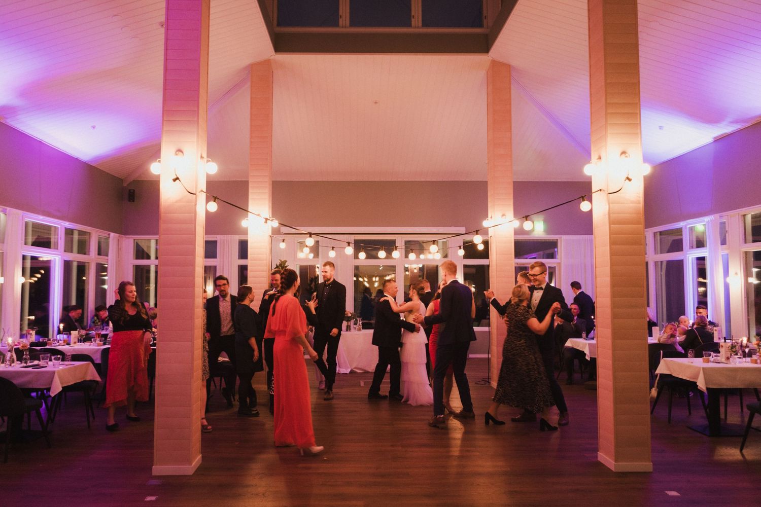 Large wedding reception venue with white columns and purple mood lighting.