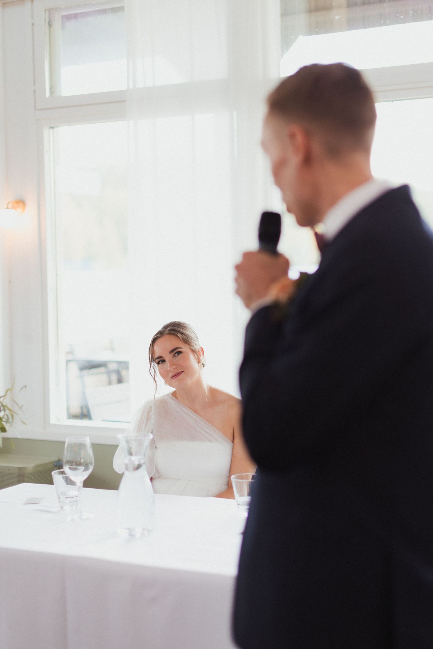 Elegant wedding reception scene with white tablecloths and natural window lighting.