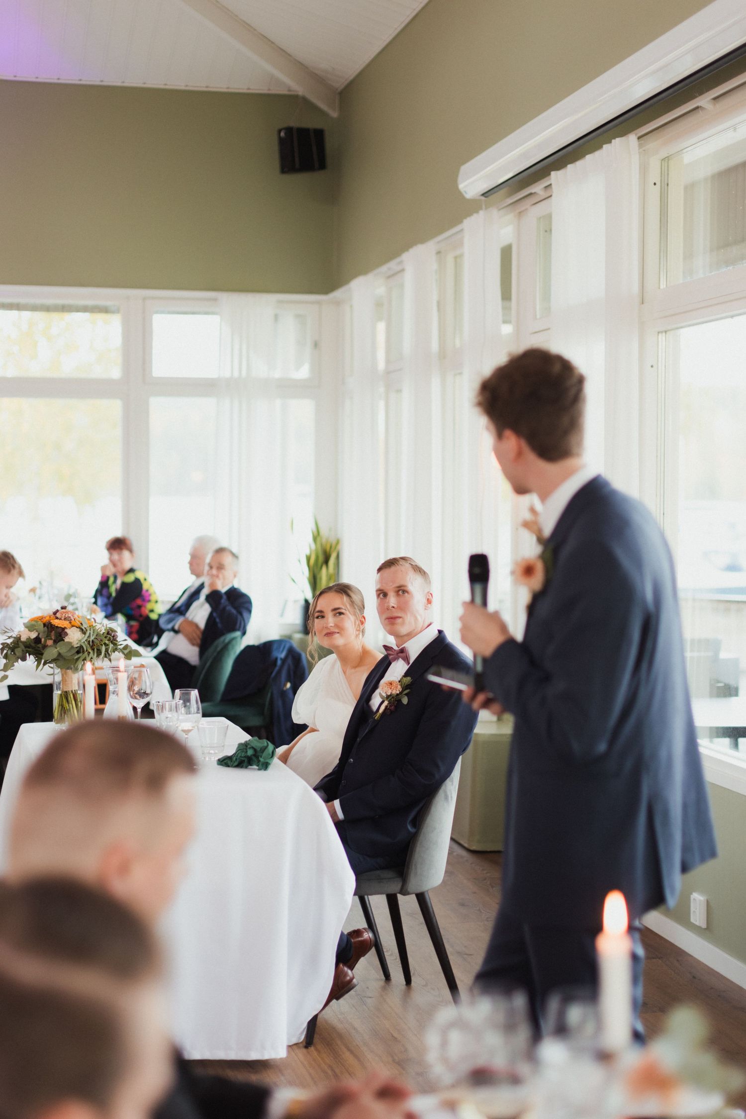 Wedding reception guests mingle and socialize in an elegant room with natural lighting.