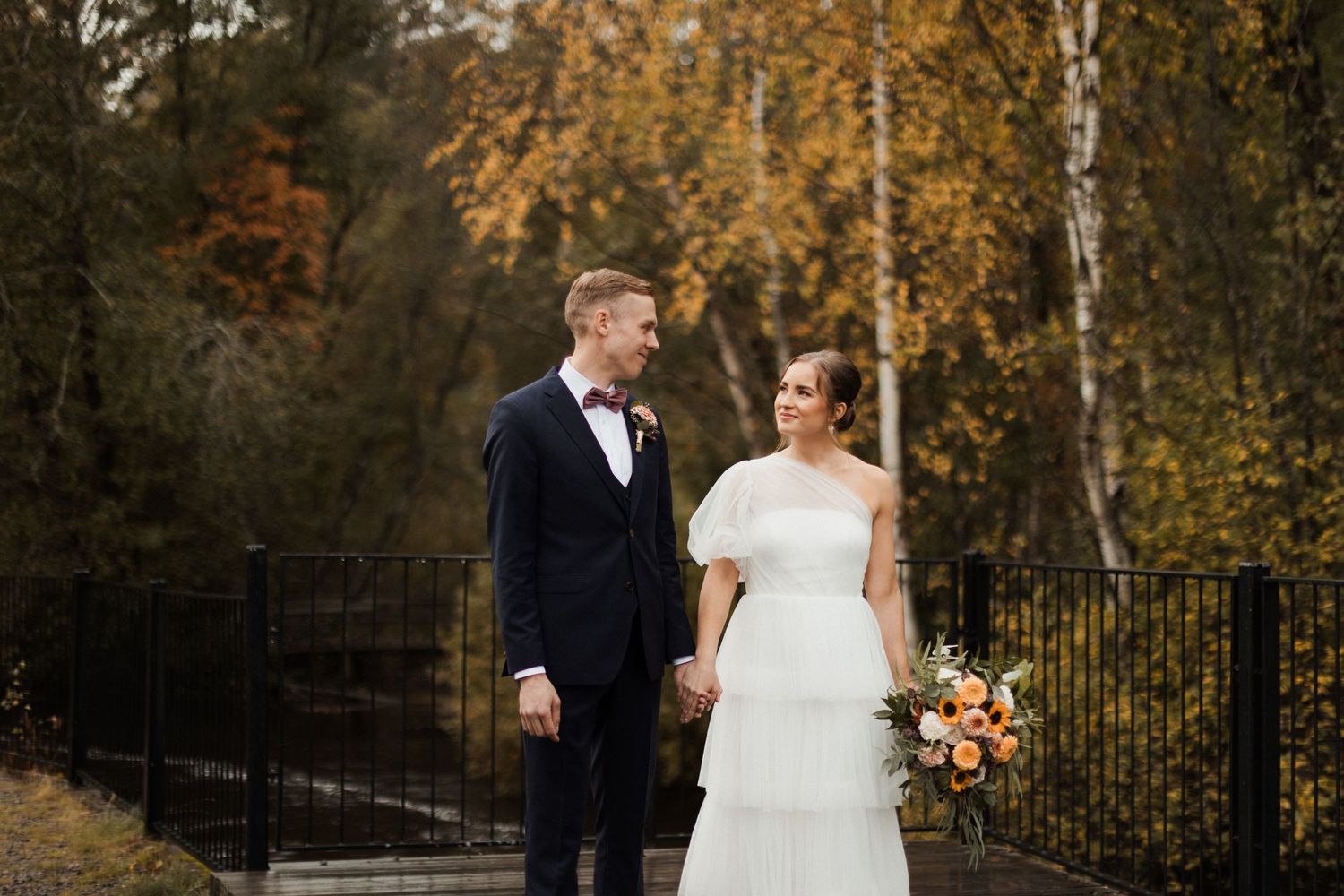 Newlyweds walking together in an autumn setting with golden foliage and white umbrellas.