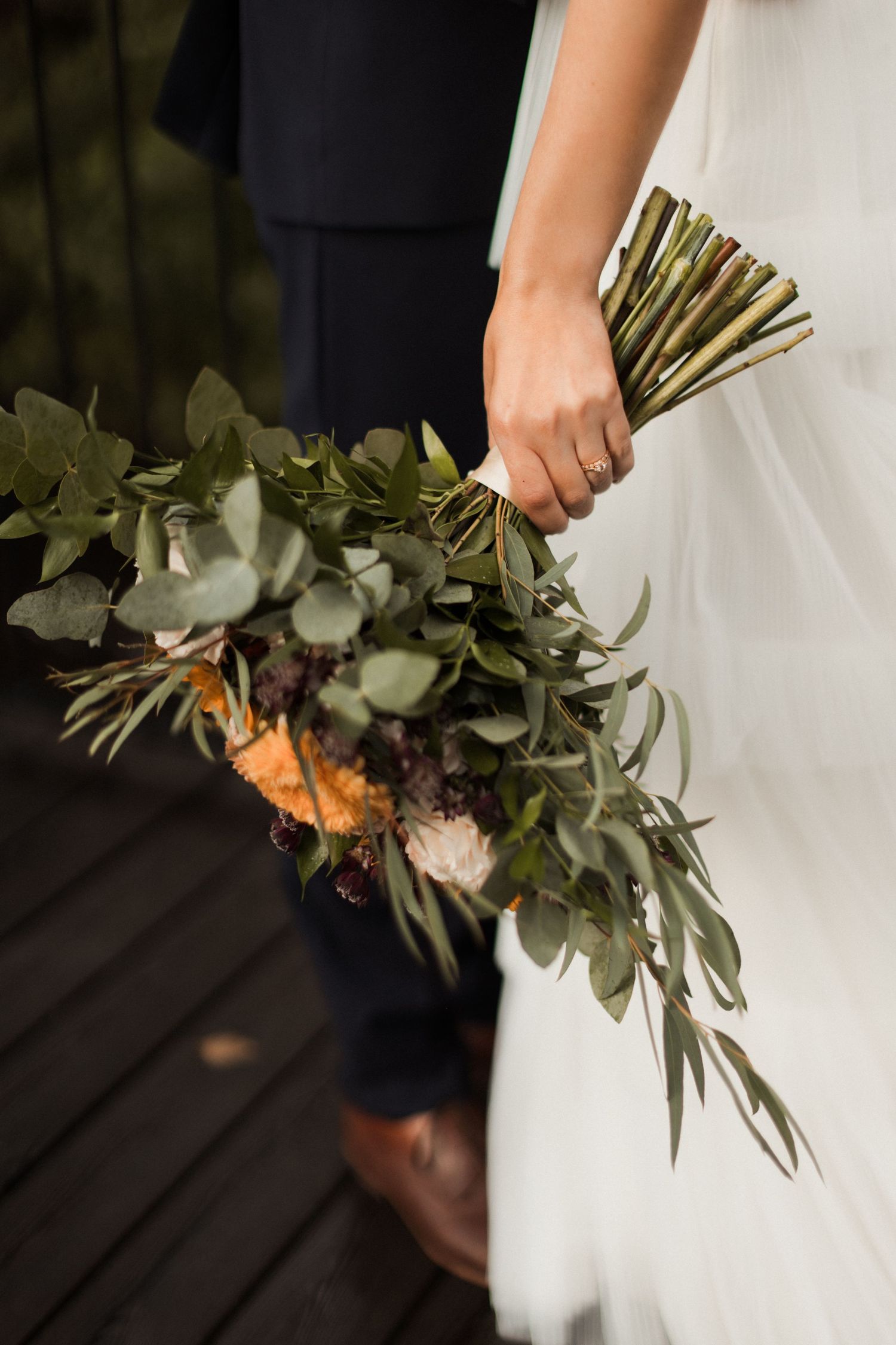 Wedding bouquet with eucalyptus leaves and orange flowers held against a white dress.