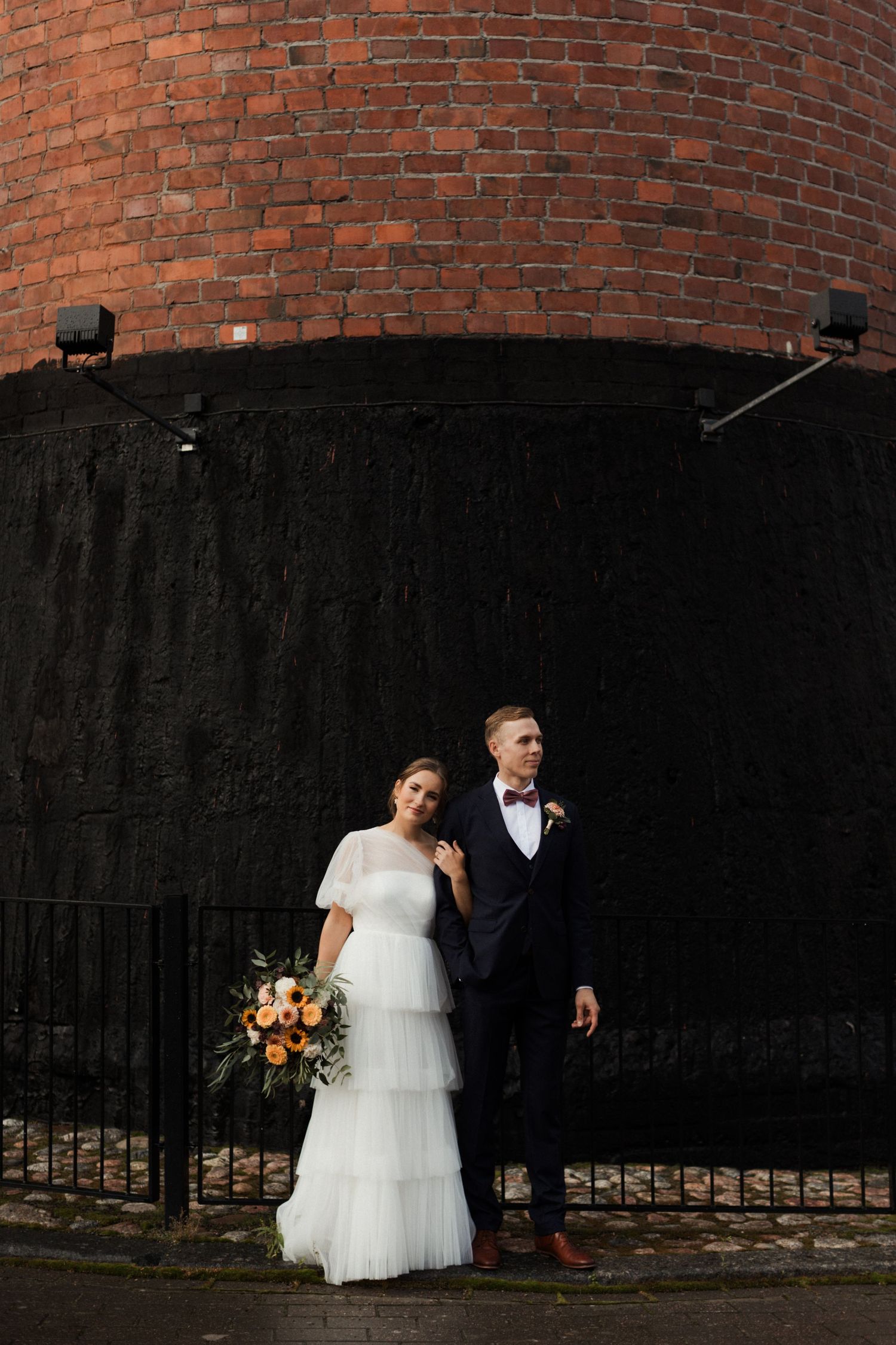 Artistic wedding photo against a dramatic red brick wall with dark shadows.