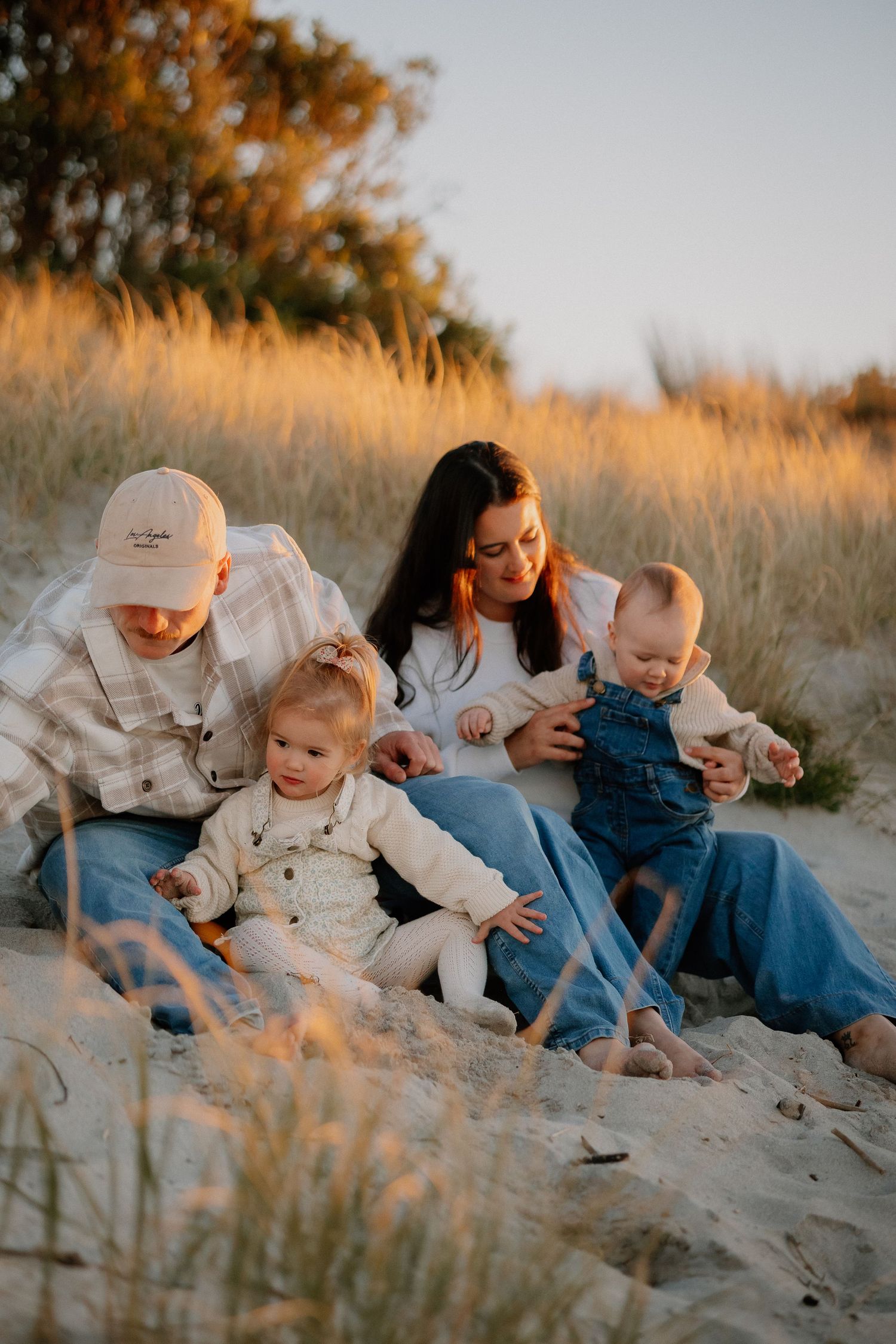 Family enjoying intimate moments together while walking on a sandy beach at sunset during golden hour.