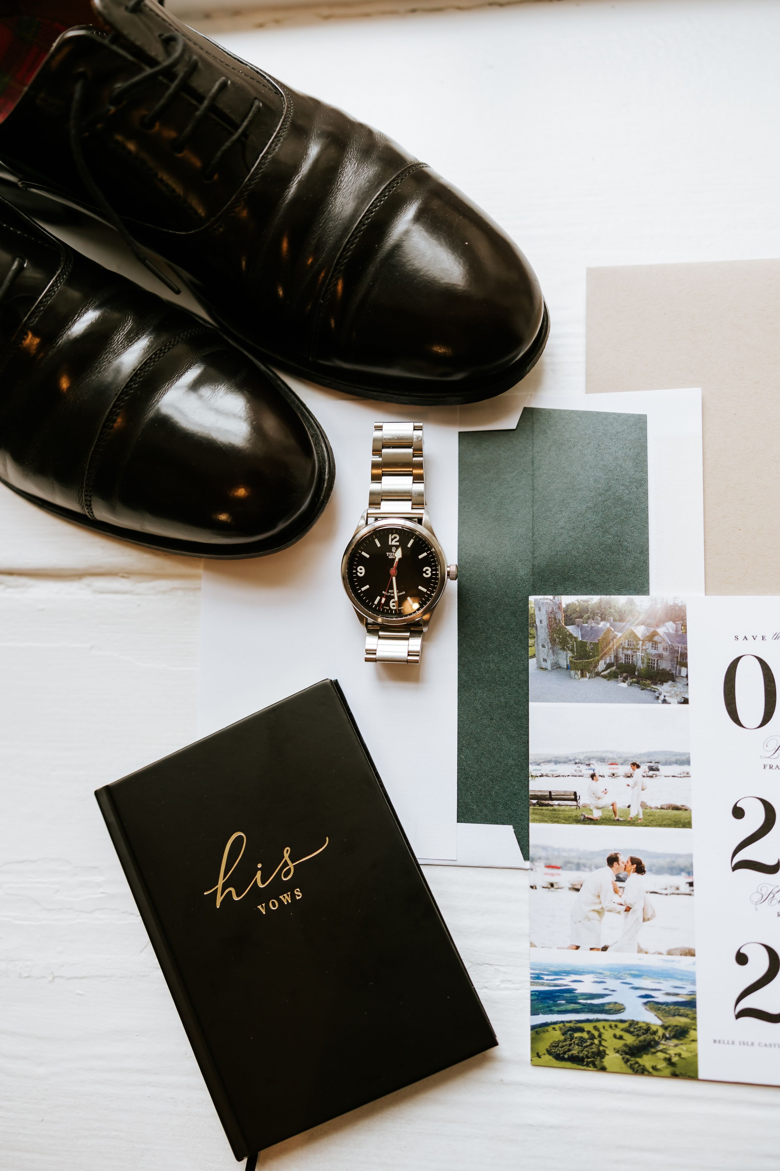A sleek black leather dress shoe sits alongside a wristwatch and photo album in an elegant minimalist composition.