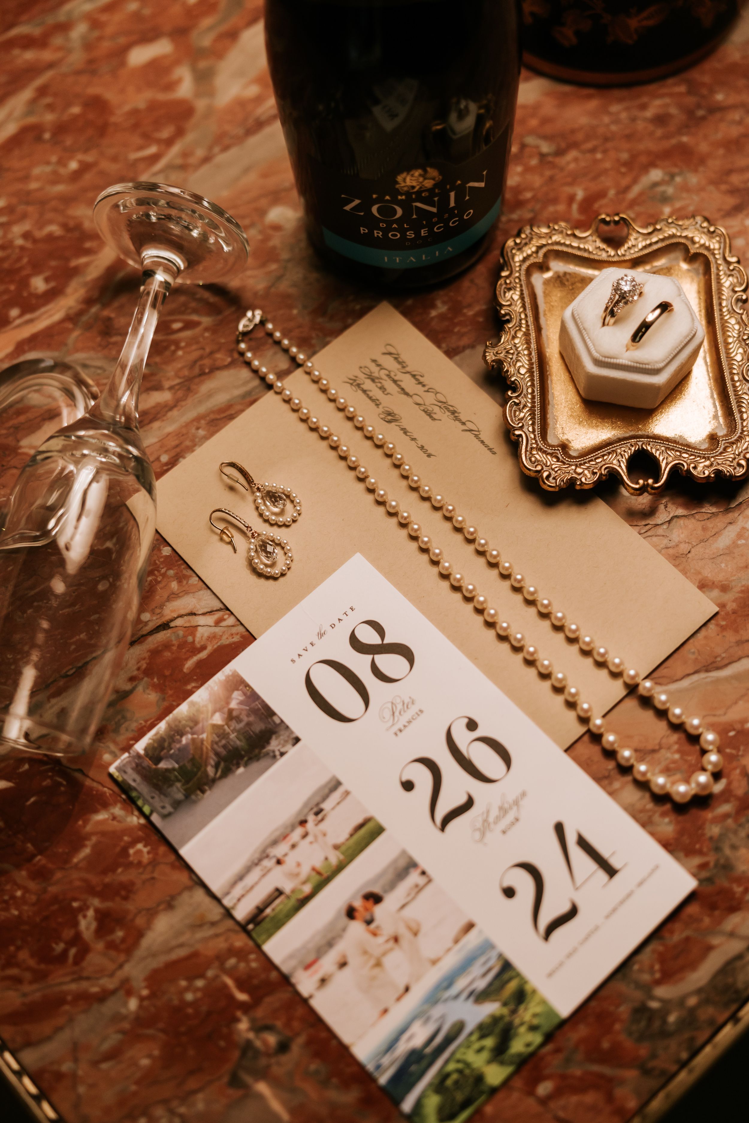 Elegant wedding reception table numbers with beaded accents and decorative designs sit on a marble surface next to wine bottles.