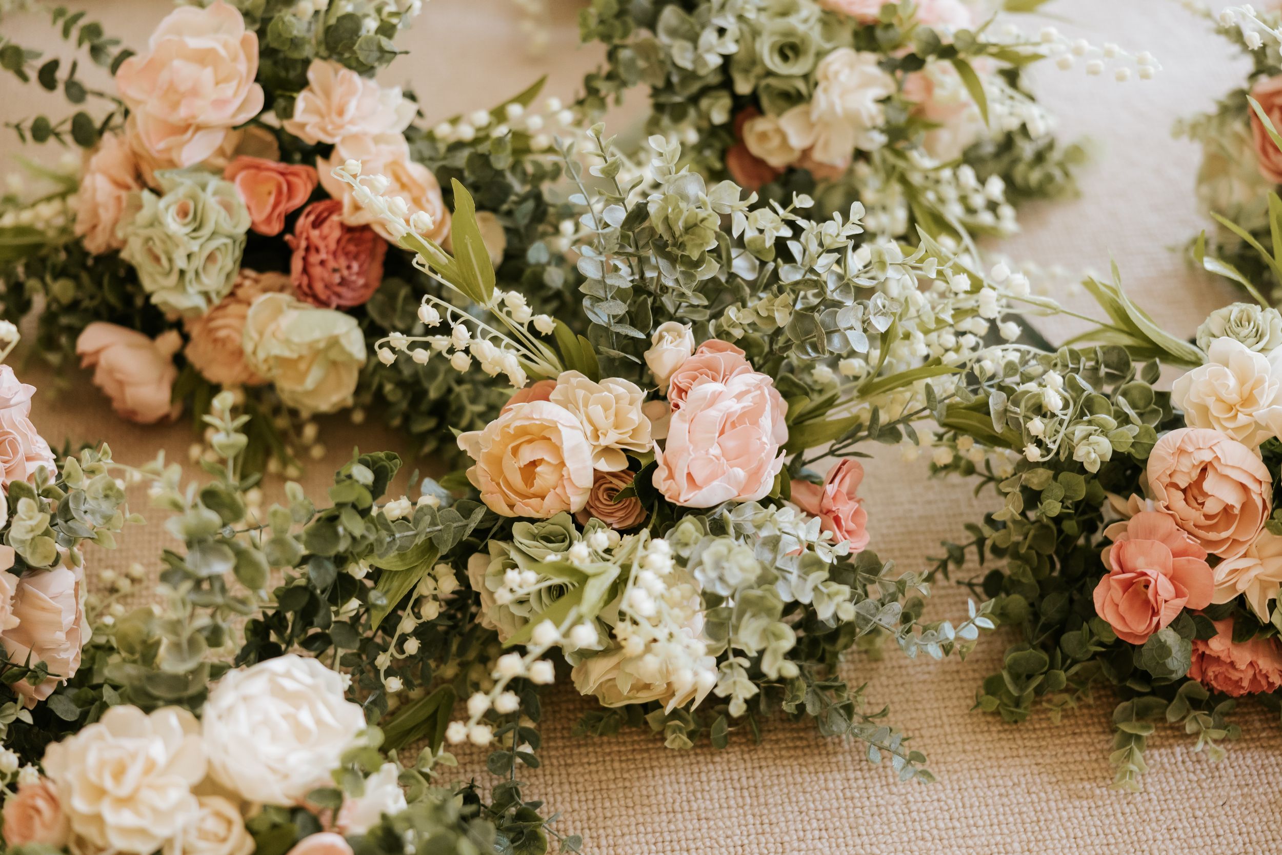 A beautiful floral wedding arch arrangement with coral roses, white baby's breath, and greenery against a soft background.
