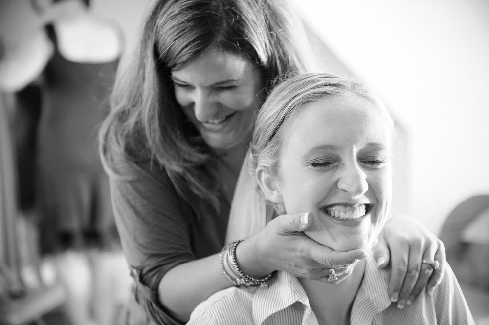 Black and white candid photo of a bride and her mother capturing joyful laughter and embraces.