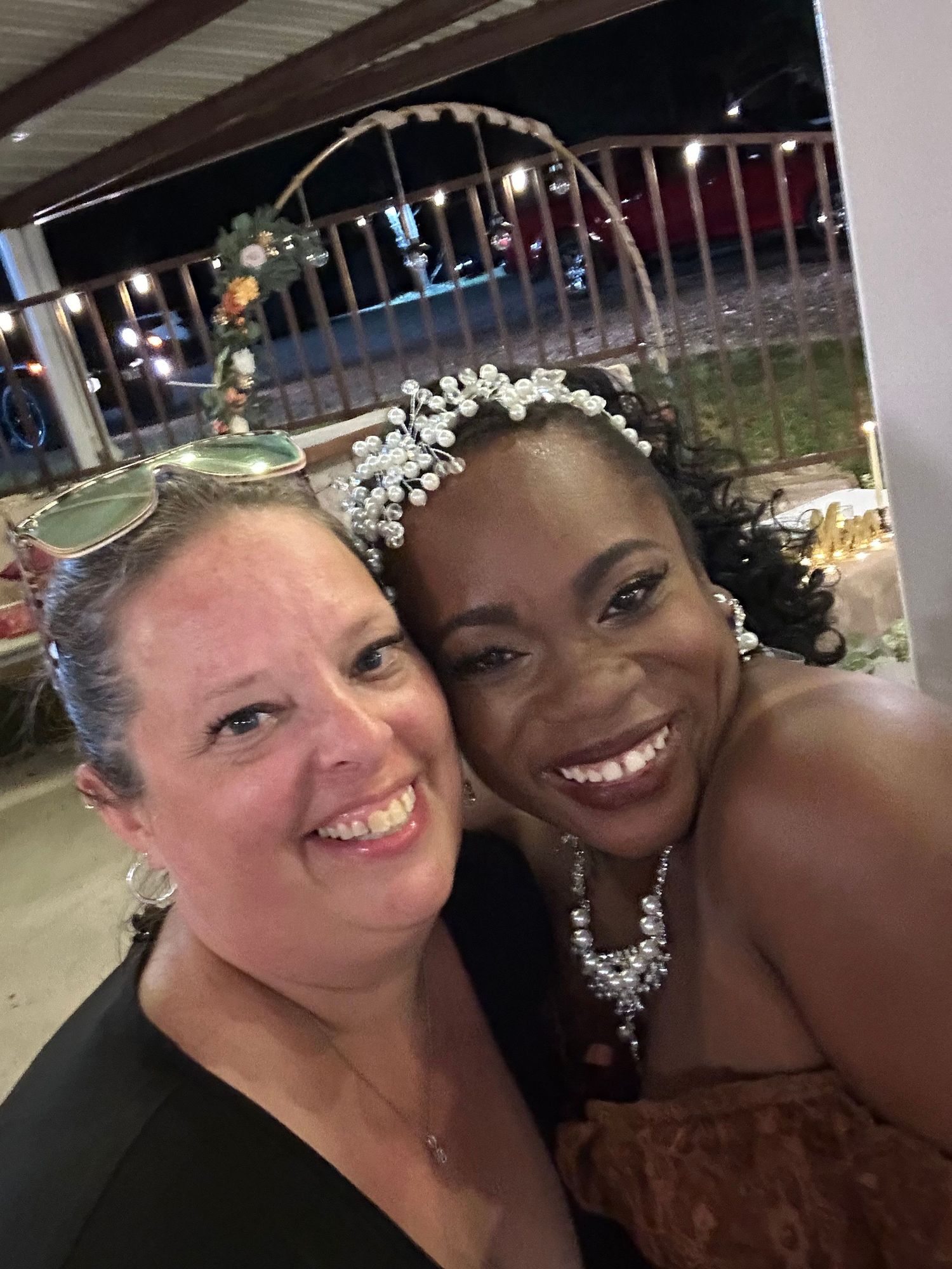 Two friends share a joyful moment at an evening event, wearing elegant accessories and bright smiles.