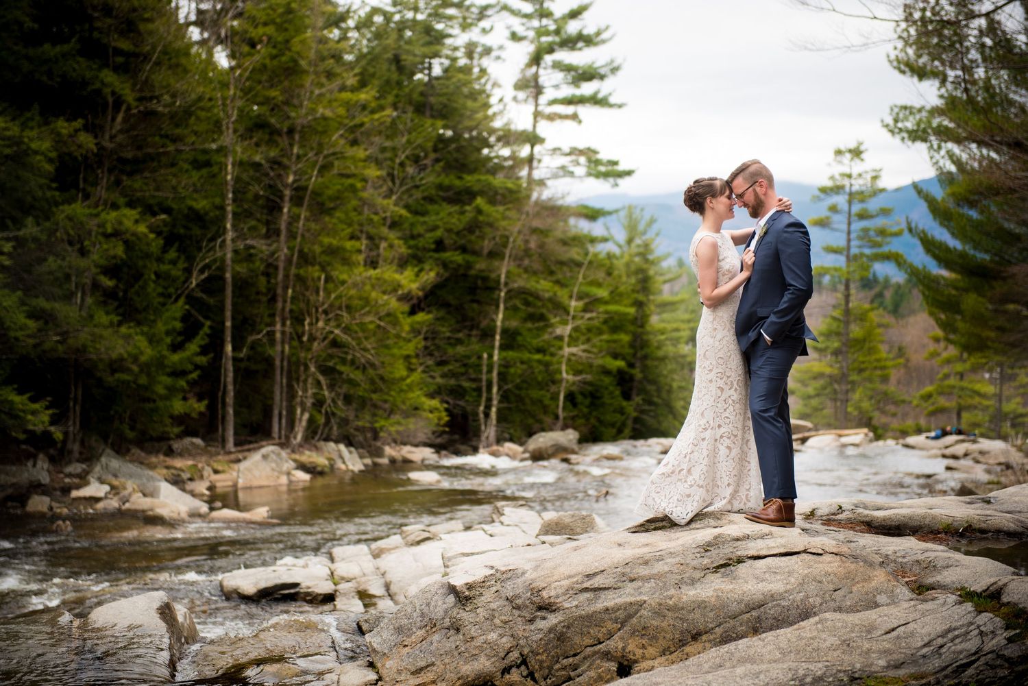Wedding couple posing on rocky terrain with evergreen forest backdrop.