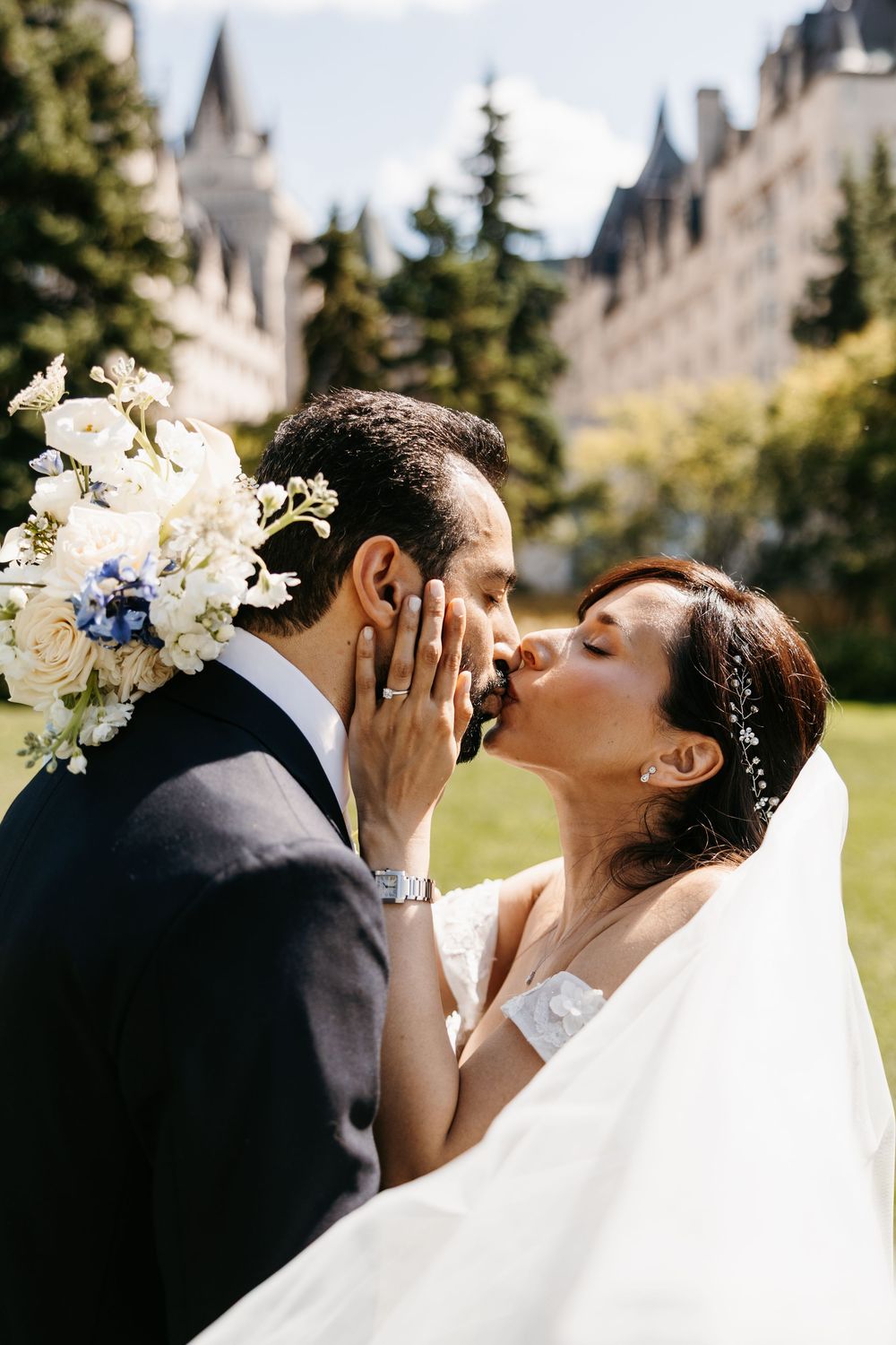 A bride and groom share a tender romantic moment while kissing outdoors with architectural elements in the background.
