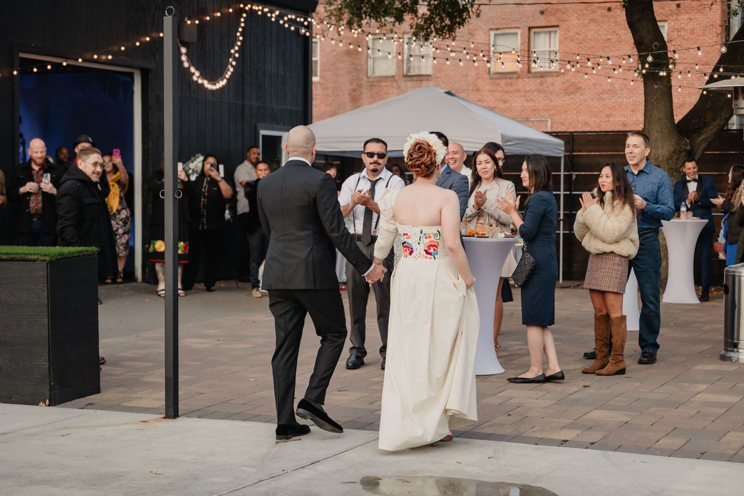 Wedding guests mingle and socialize at cocktail hour decorated with string lights and brick architecture for Sacramento wedding