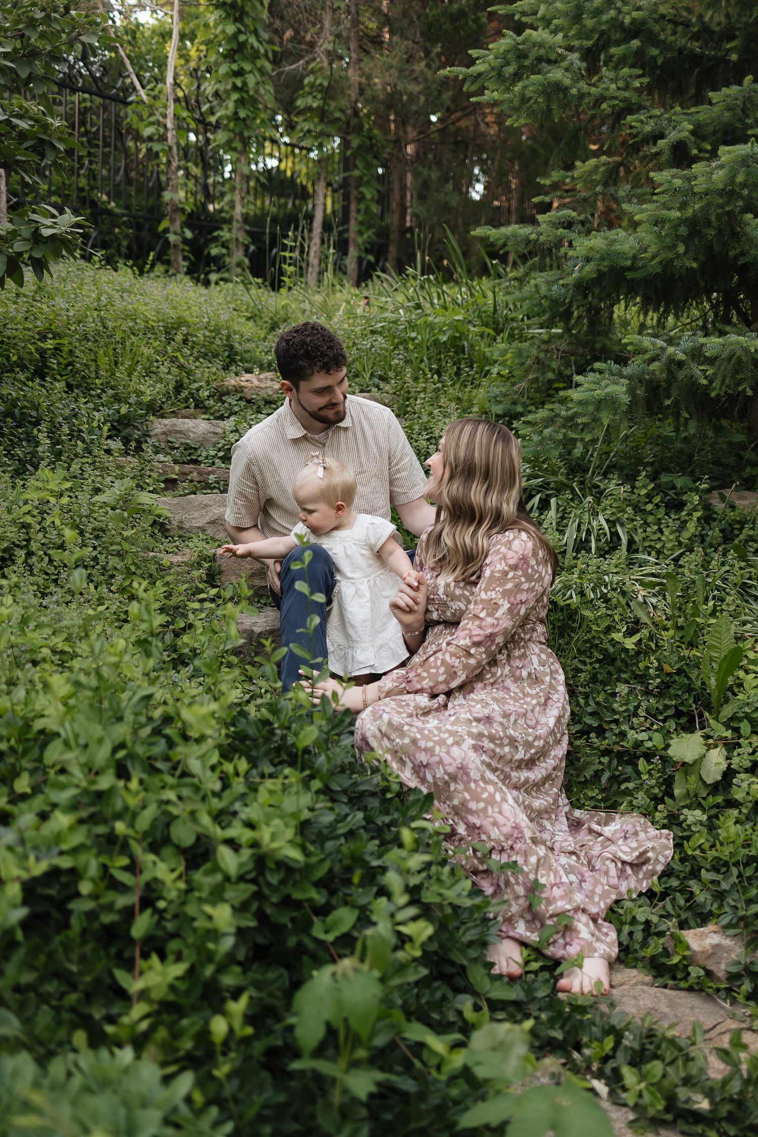family sitting on staggered stones surrounded by green vines at the sunken garden Family photographers kansas city