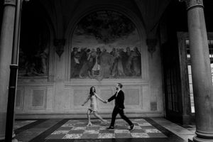 Black and white architectural scene showing people walking through an ornate corridor.