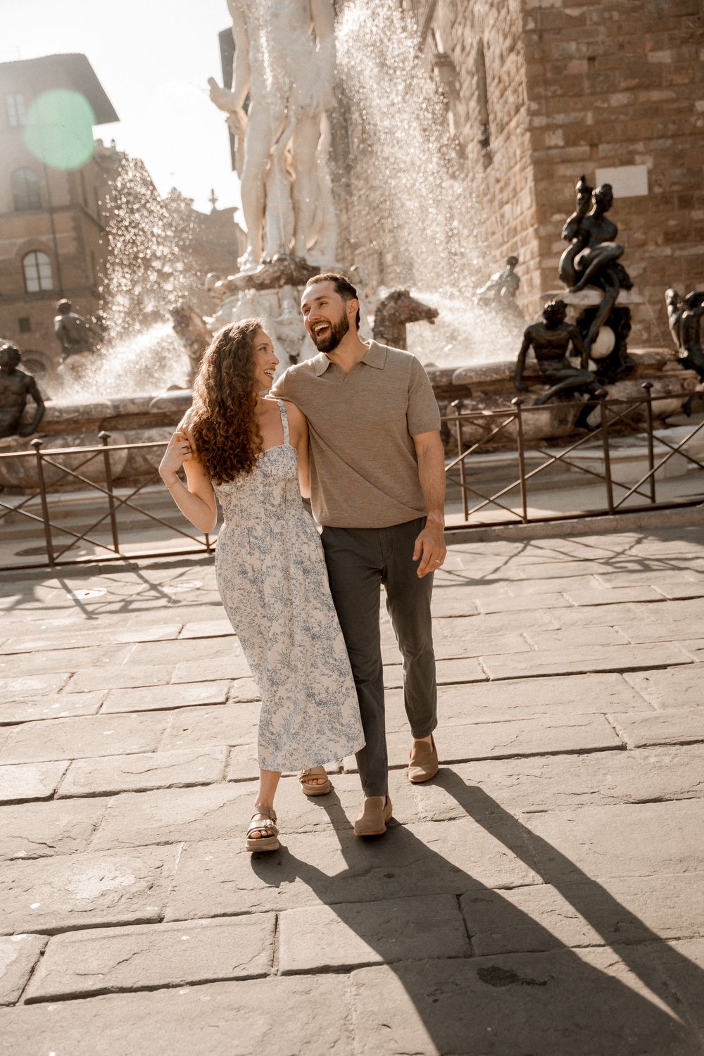 Couple walking together on stone pavement casting long shadows in warm sunlight at Palazzo Vecchio in Florence.