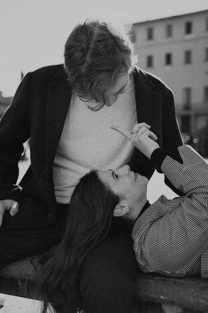 Black and white portrait of couple in playful intimate moment on bench.