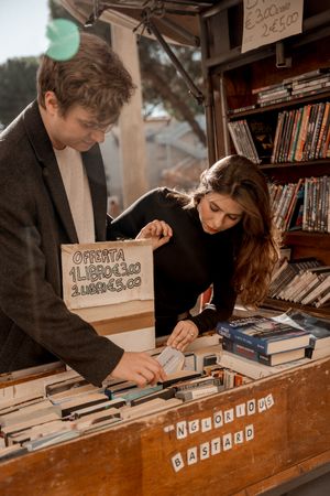 Couple browsing vintage books together at outdoor bookstore stall.