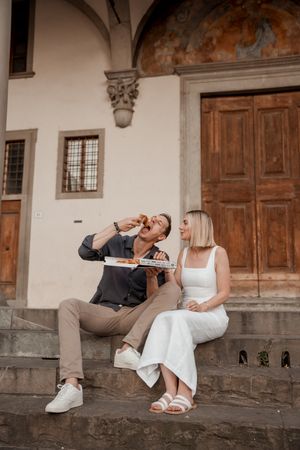 A couple sitting and leaning back on stone steps in front of historic architecture.