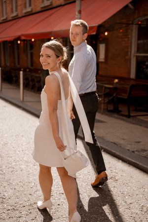 Close-up view of bride and groom's legs walking on a sunny cobblestone street near brick buildings.