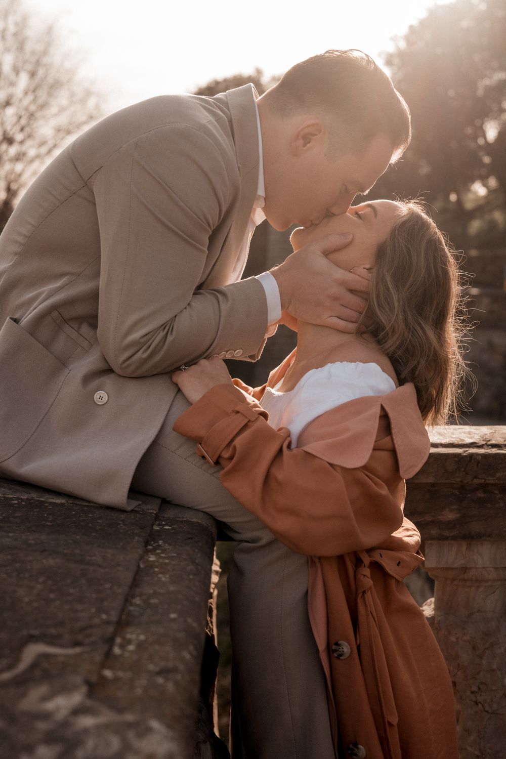 Intimate couple sharing romantic moment in warm sunlight against stone wall backdrop.