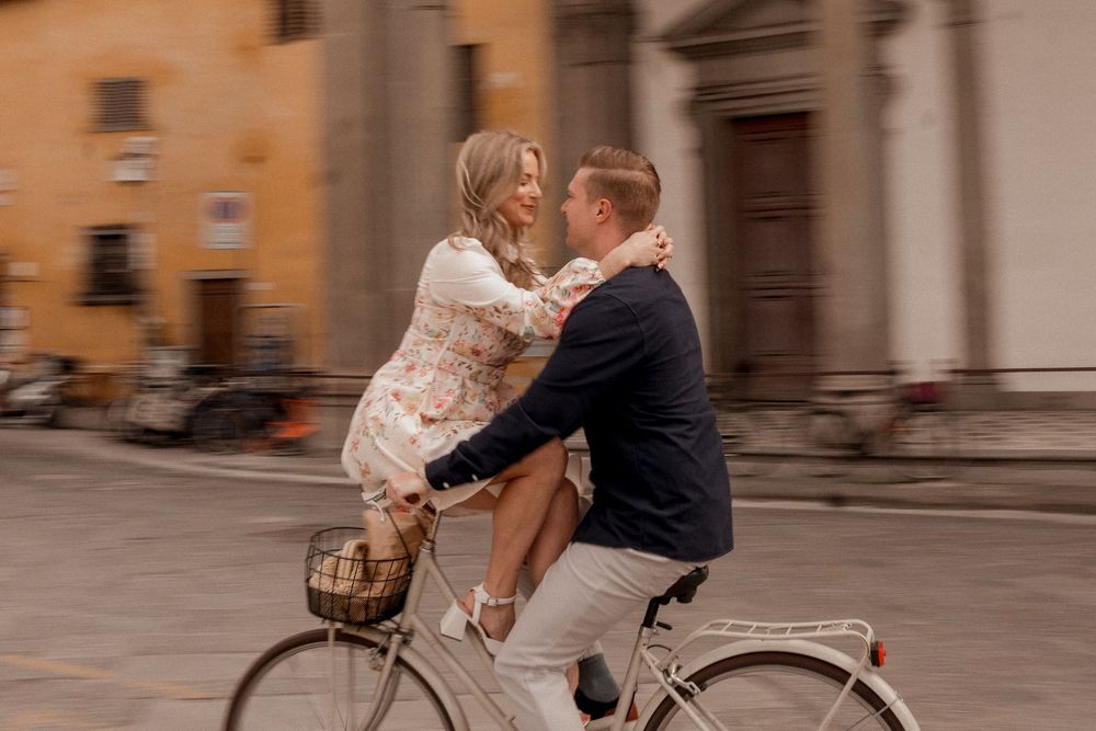 Playful couple riding vintage bicycle together through Italian streets.