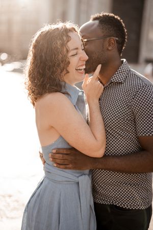 Couple laughing and embracing in golden sunlight during romantic photoshoot.