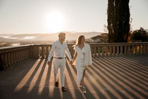 Couple walking hand in hand on terrace at sunset casting long shadows in Italy