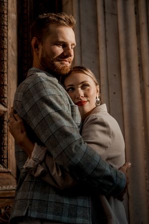 Couple embracing in moody lighting against rustic wall backdrop.