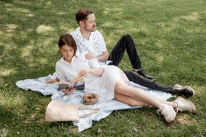 A couple relaxes on a picnic blanket in a grassy park on a sunny afternoon.